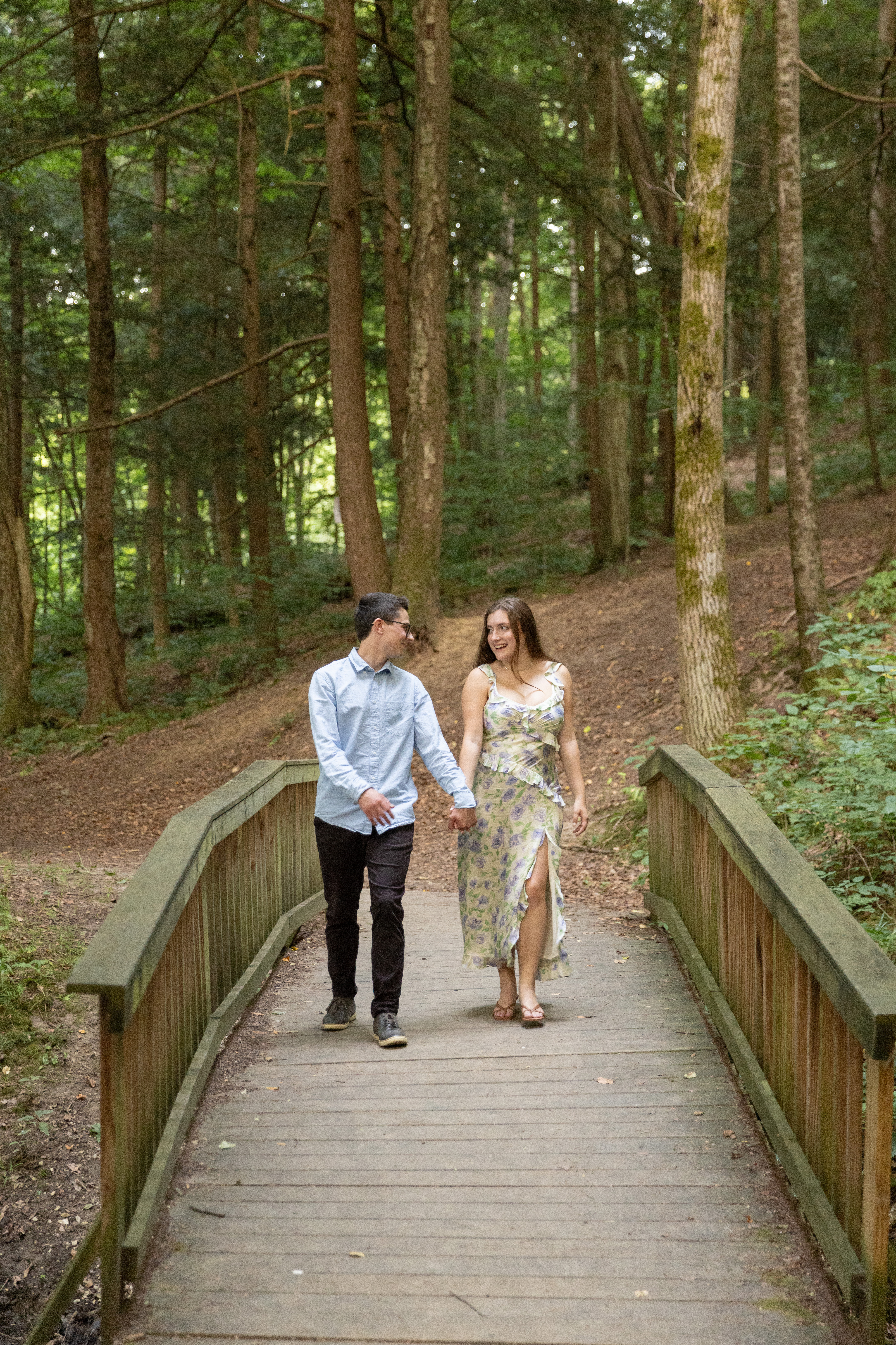 Syl and Sarah walking hand in hand across a footbridge in the woods